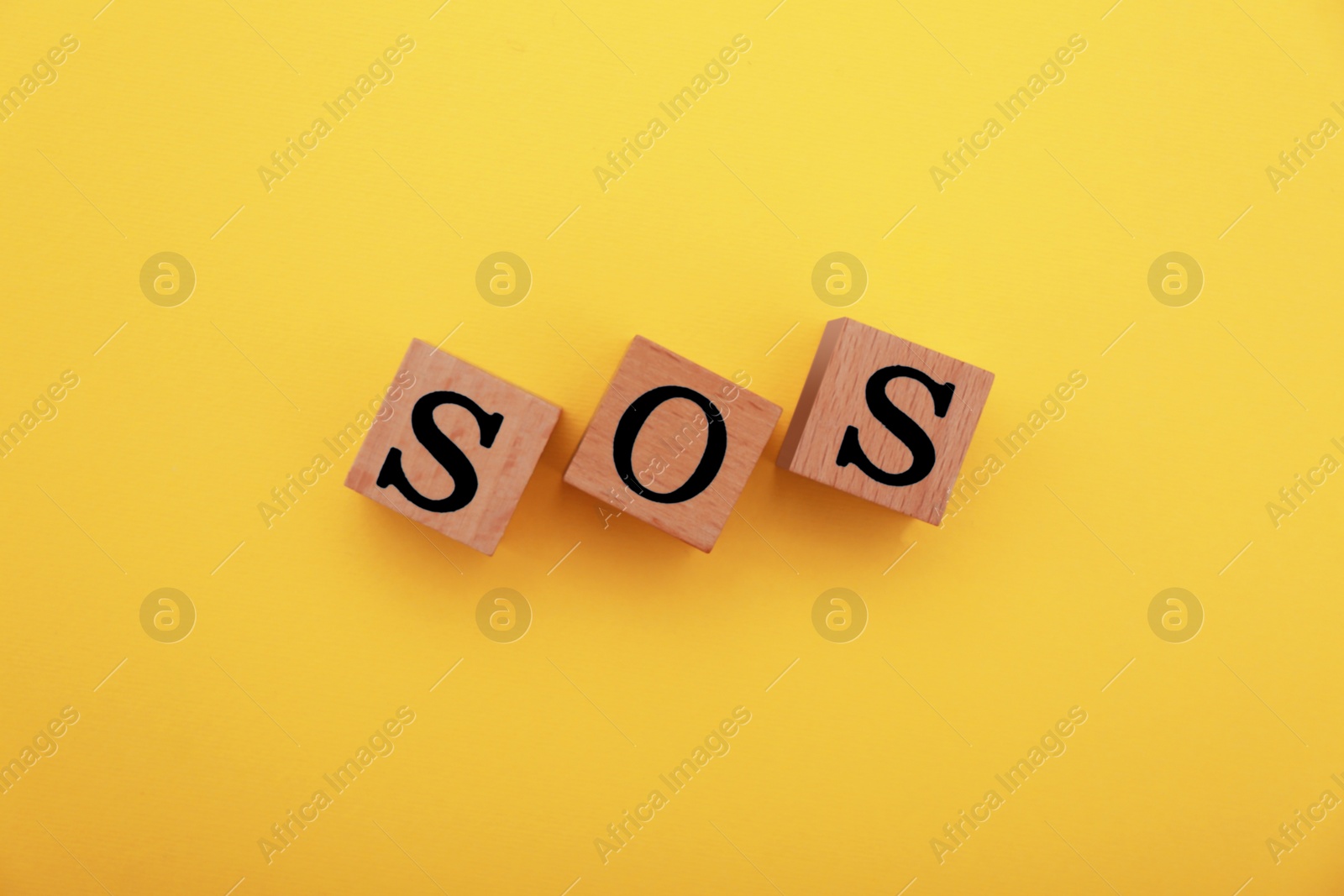 Photo of Abbreviation SOS made of wooden cubes on yellow background, top view