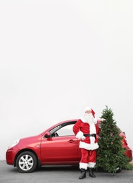 Photo of Authentic Santa Claus with Christmas tree near red car, outdoors