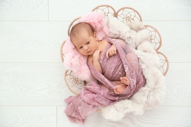Photo of Adorable newborn girl lying in baby nest on light background, top view