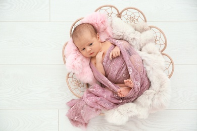 Adorable newborn girl lying in baby nest on light background, top view