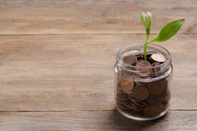 Glass jar with coins and flower on wooden table, space for text. Investment concept