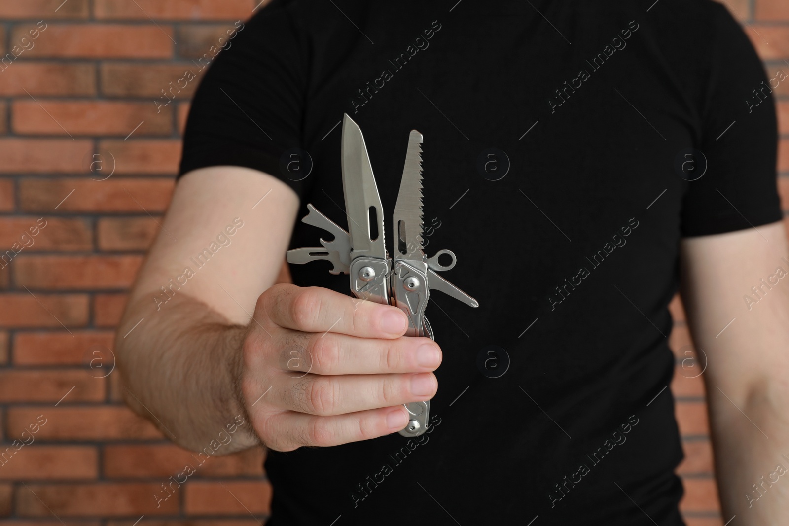 Photo of Man holding multitool near brick wall, closeup