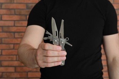 Man holding multitool near brick wall, closeup