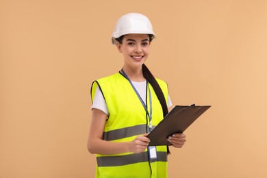 Photo of Engineer in hard hat holding clipboard on beige background