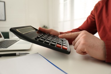 Man using calculator at table indoors, closeup