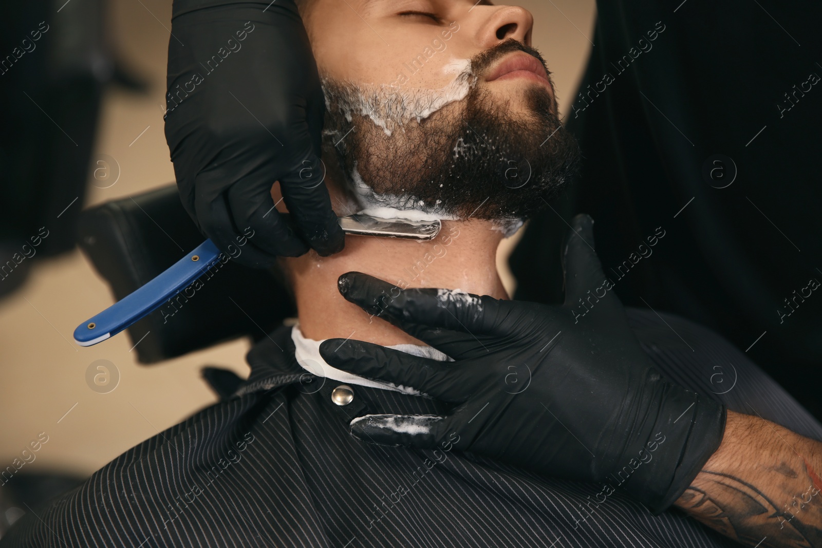 Photo of Professional hairdresser shaving client with straight razor in barbershop