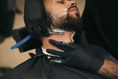 Professional hairdresser shaving client with straight razor in barbershop