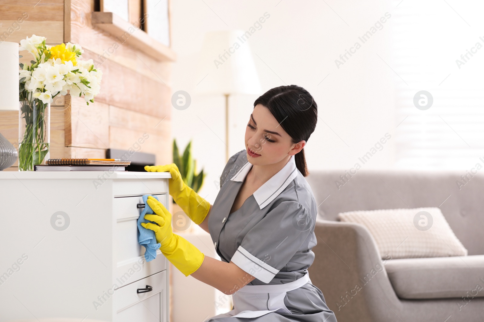 Photo of Young chambermaid wiping dust from furniture in hotel room