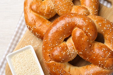 Delicious pretzels and bowl with sesame seeds on white wooden table, flat lay