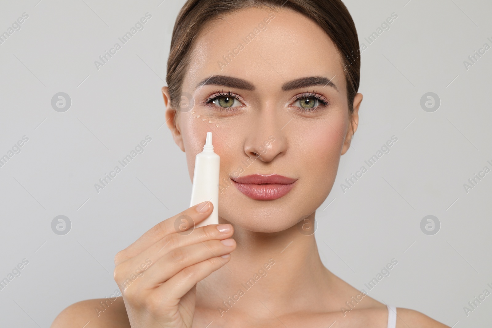 Photo of Young woman applying cream under eye on white background