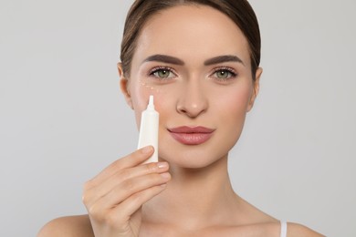 Young woman applying cream under eye on white background