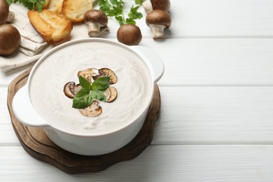 Photo of Delicious homemade mushroom soup in ceramic pot, croutons, fresh champignons and parsley on white wooden table. Space for text