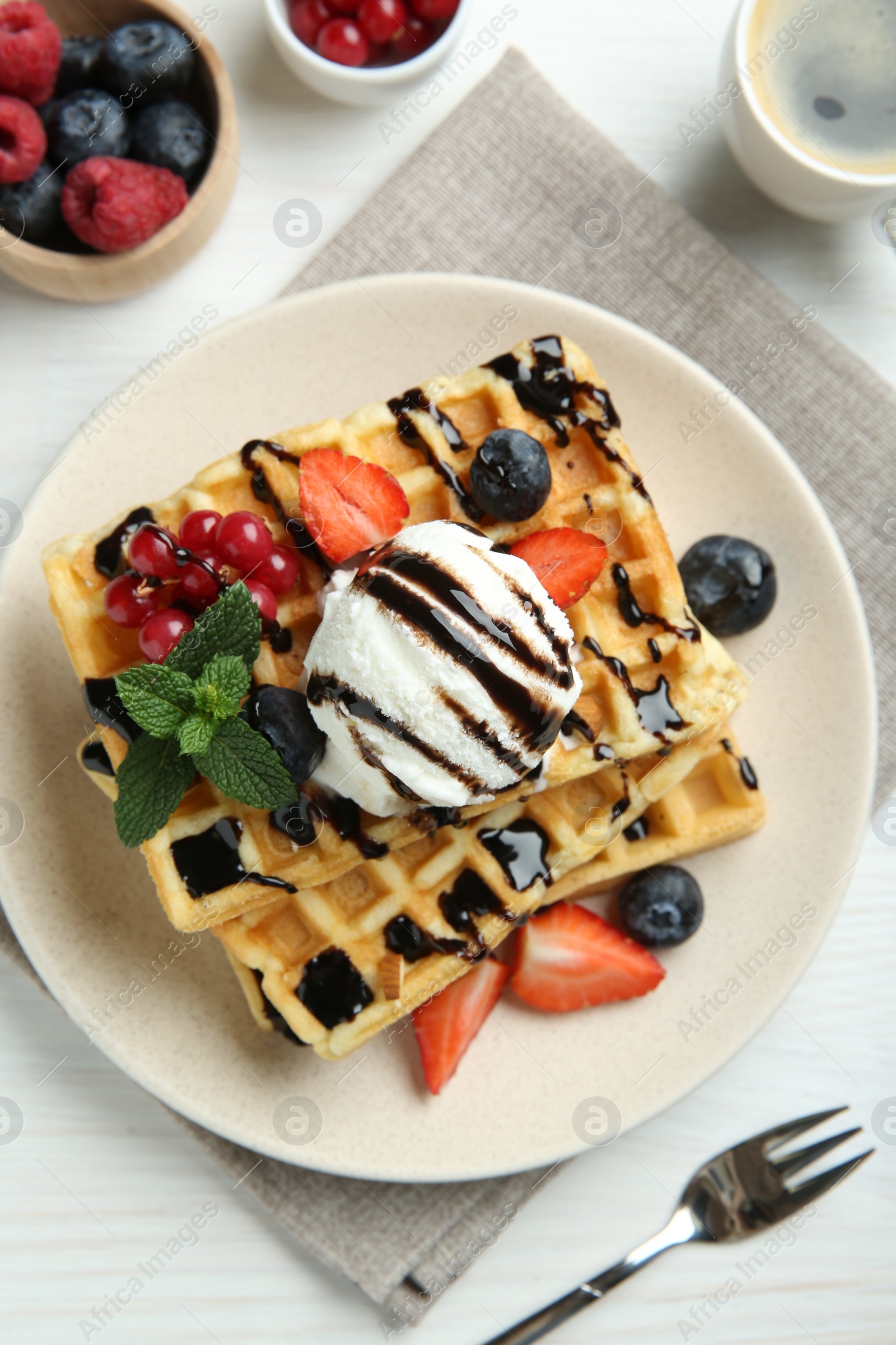 Photo of Delicious Belgian waffles with ice cream, berries and chocolate sauce served on white wooden table, flat lay