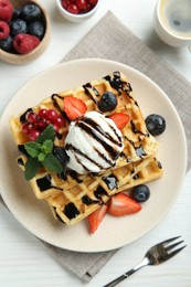 Delicious Belgian waffles with ice cream, berries and chocolate sauce served on white wooden table, flat lay