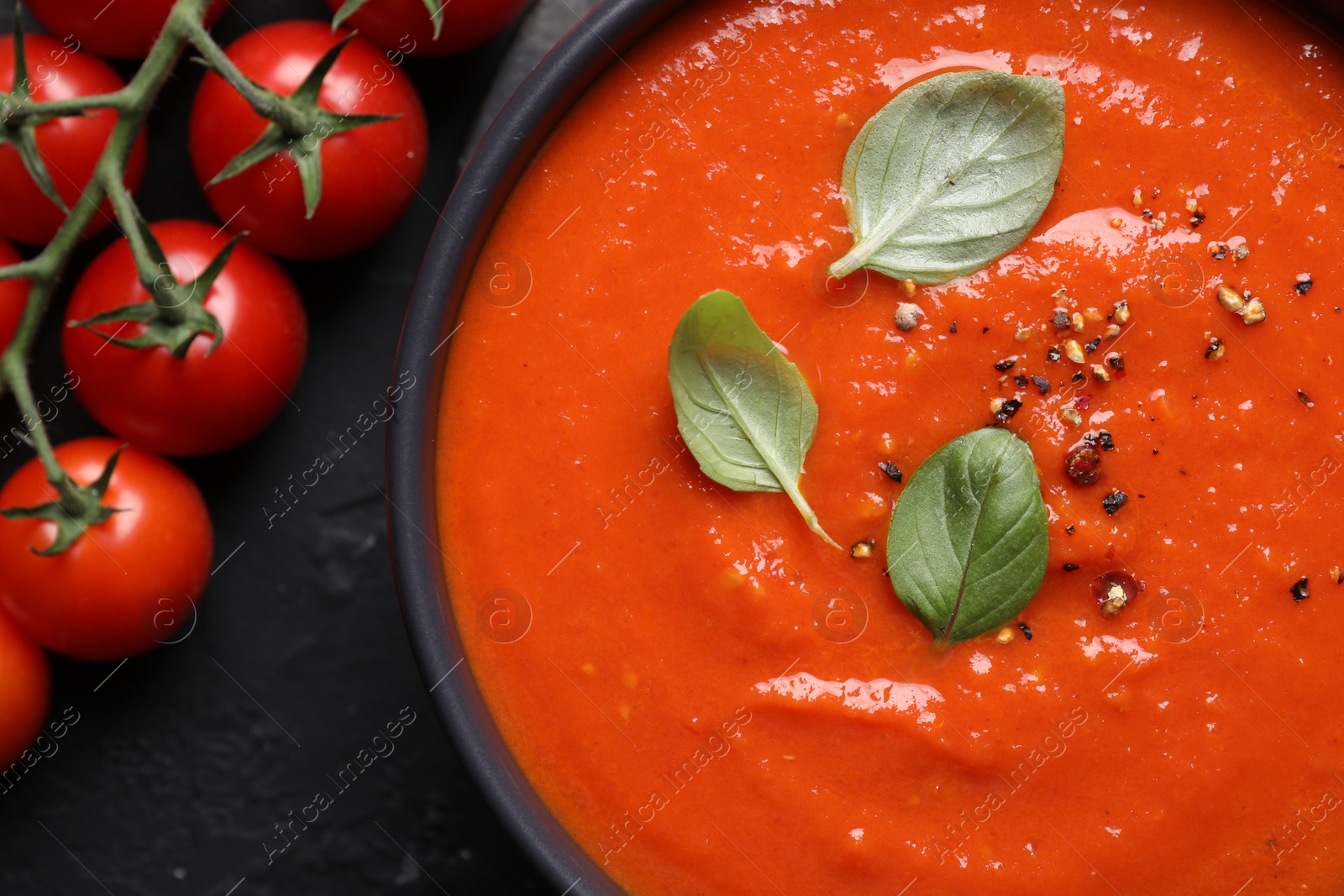 Photo of Delicious tomato cream soup and fresh fruits on black textured table, top view