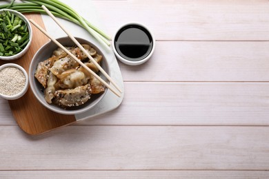 Delicious gyoza (asian dumplings), soy sauce, green onion and sesame on white wooden table, flat lay. Space for text