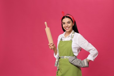 Photo of Young housewife in oven glove holding rolling pin on pink background. Space for text