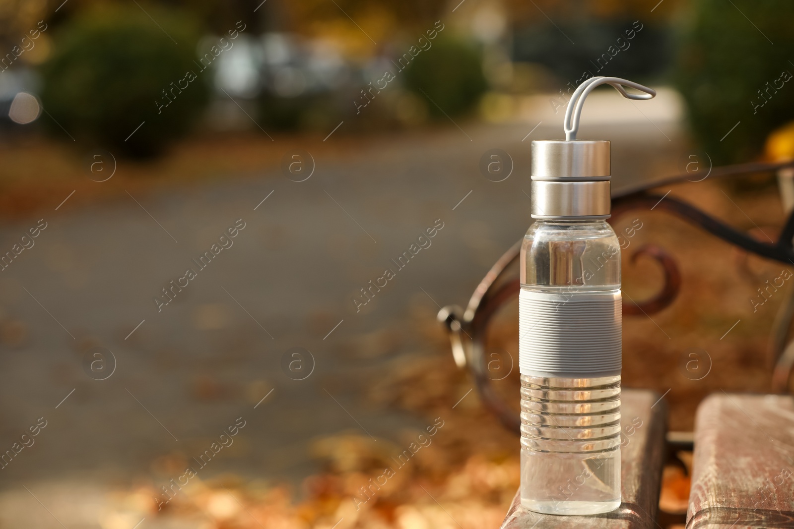 Photo of Sport bottle of water on wooden bench in park, space for text