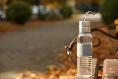 Sport bottle of water on wooden bench in park, space for text