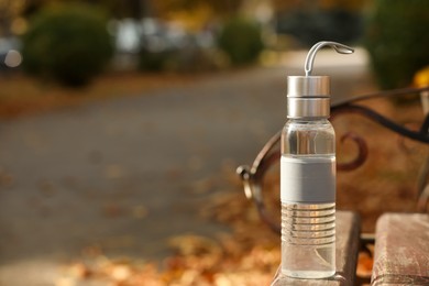 Photo of Sport bottle of water on wooden bench in park, space for text