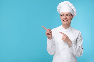 Happy woman chef in uniform pointing at something on light blue background, space for text