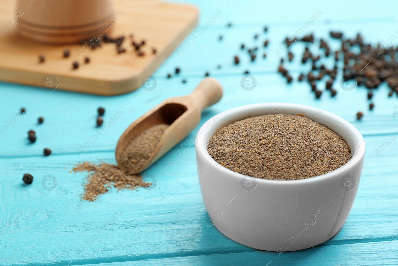 Photo of Bowl of black pepper powder and scoop on blue wooden table, space for text