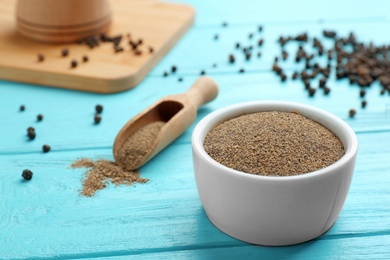 Bowl of black pepper powder and scoop on blue wooden table, space for text