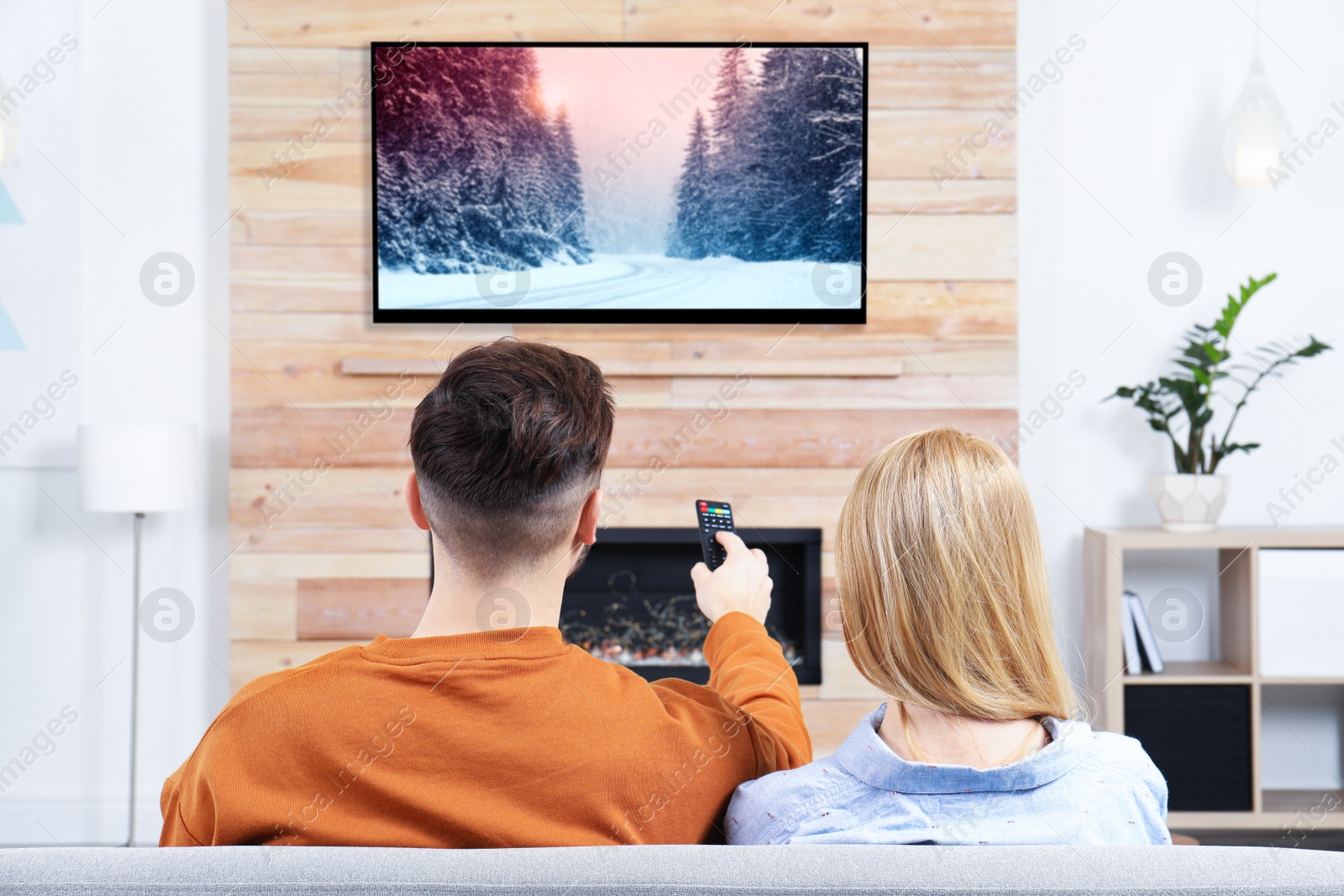 Image of Couple watching TV on sofa in living room with decorative fireplace