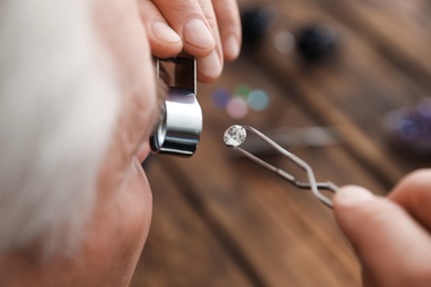 Photo of Male jeweler evaluating precious gemstone in workshop, closeup