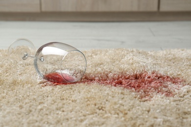 Photo of Overturned glass and spilled red wine on soft carpet