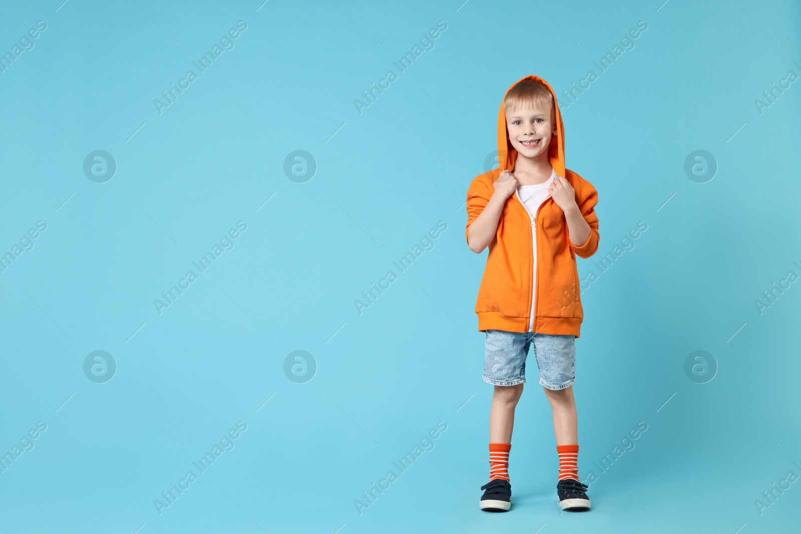 Photo of Happy little boy dancing on light blue background. Space for text