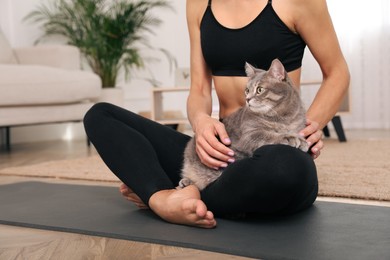 Photo of Woman stroking her cat while practicing yoga at home, closeup