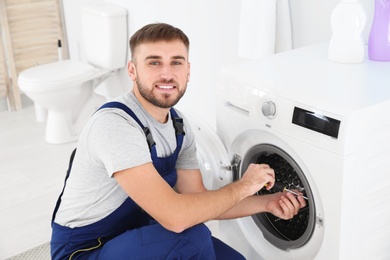 Photo of Young plumber fixing washing machine in bathroom