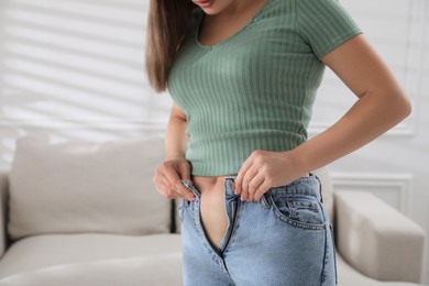 Woman trying to put on tight jeans at home, closeup. Space for text