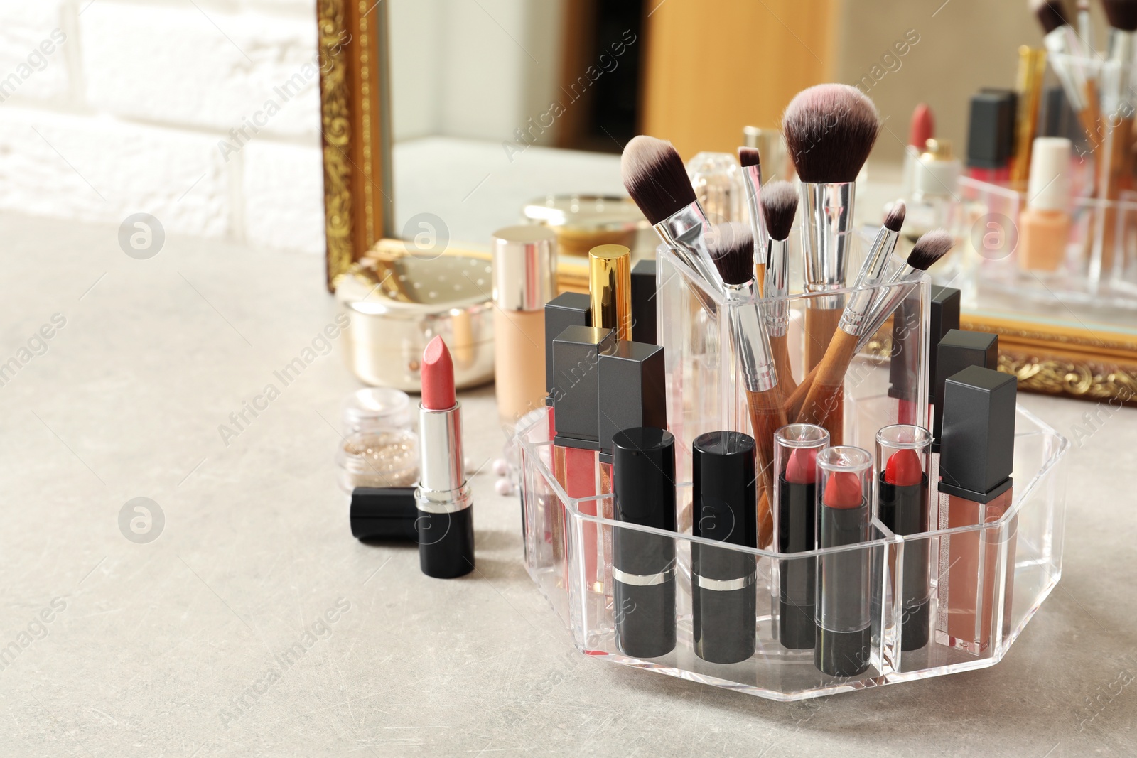 Photo of Lipstick holder with different makeup products on dressing table near mirror. Space for text