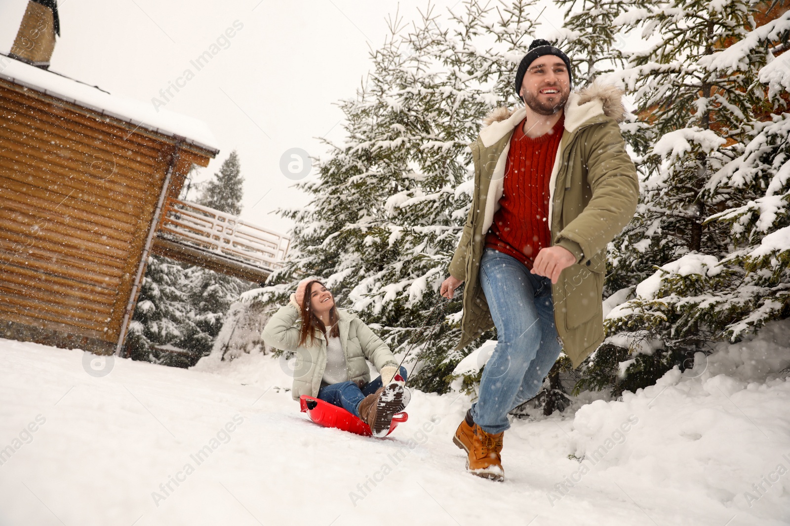 Photo of Young man pulling sled with his girlfriend outdoors on snowy day. Winter vacation