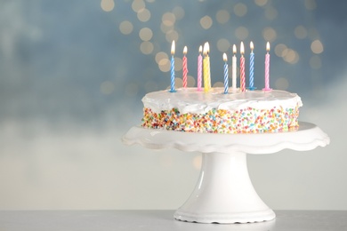 Photo of Tasty birthday cake with burning candles on table against blurred lights, space for text