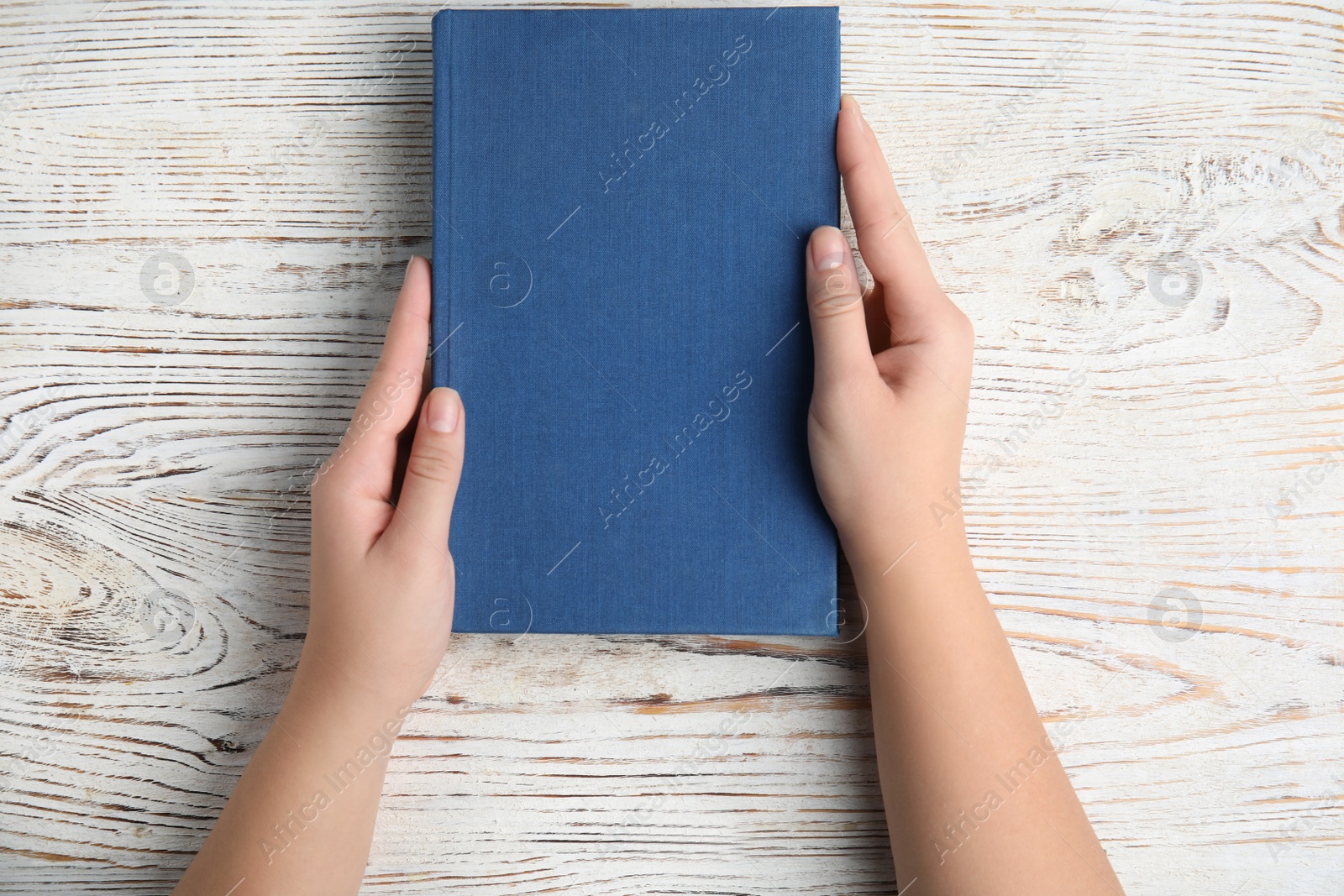 Photo of Woman holding hardcover book on white wooden background, top view