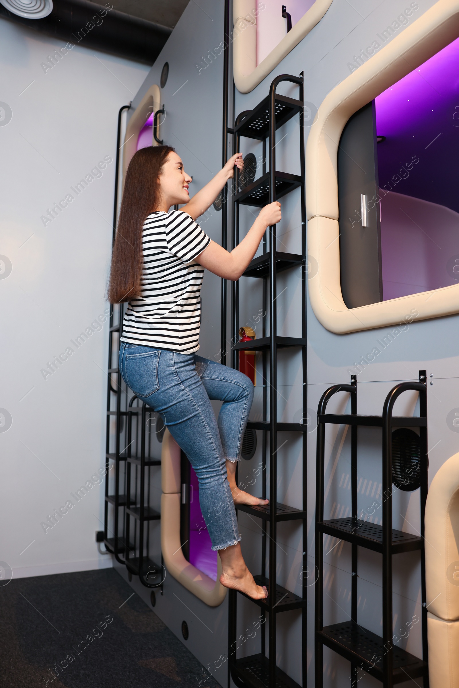 Photo of Happy young woman climbing up ladder to capsule in pod hostel