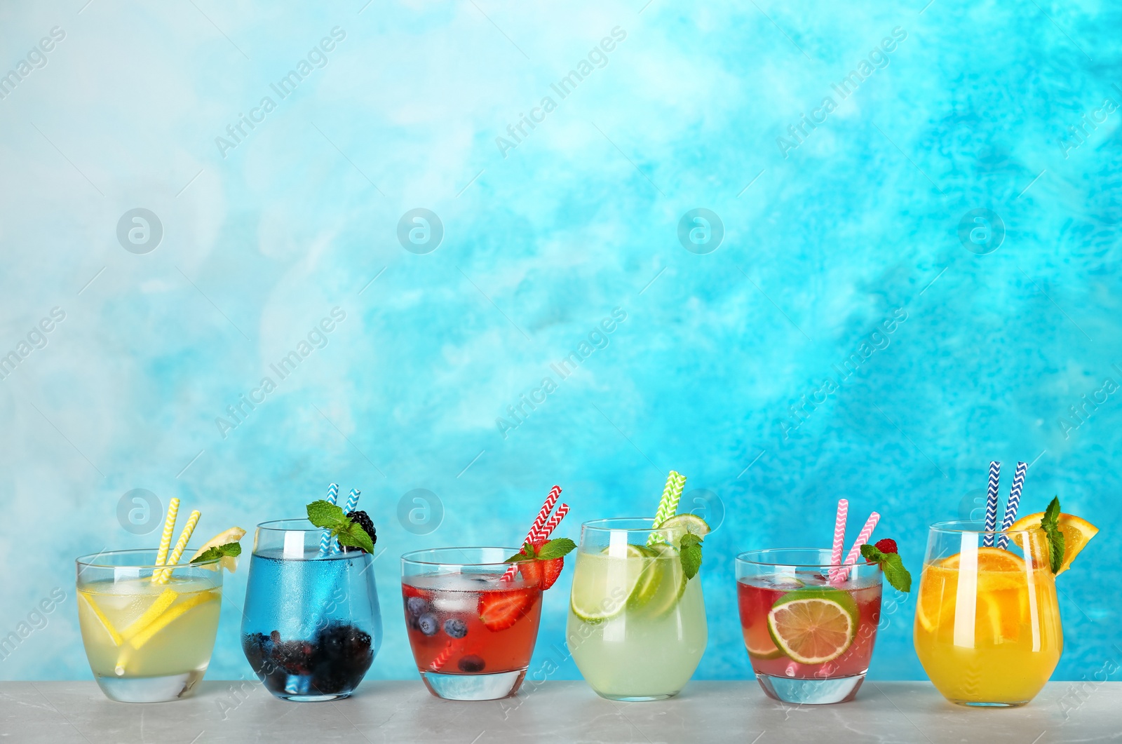 Photo of Glasses with lemonades on table against color background