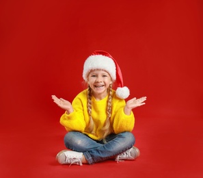 Cute little child wearing Santa hat on red background. Christmas holiday