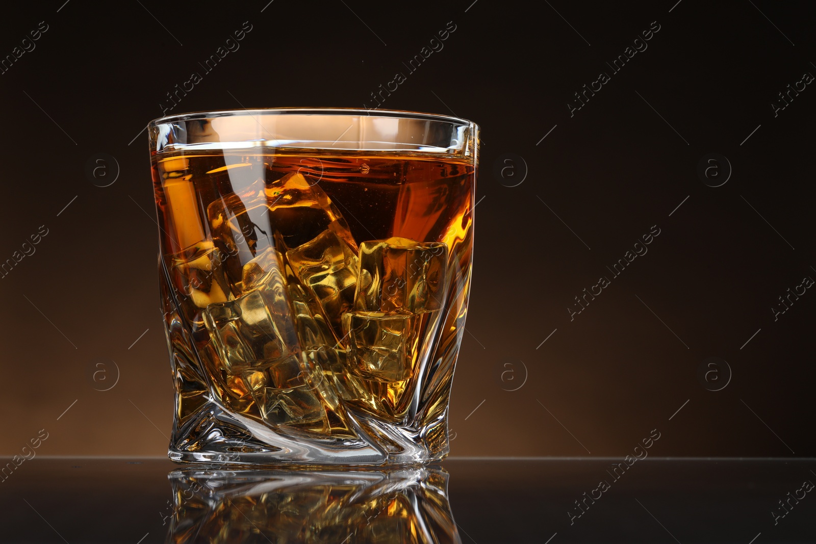 Photo of Whiskey with ice cubes in glass on table against color background, space for text