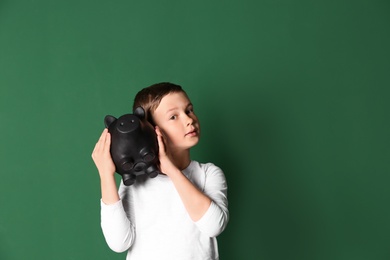 Little boy with piggy bank on color background. Space for text