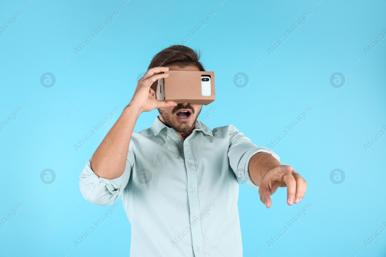 Photo of Young man using cardboard virtual reality headset on color background