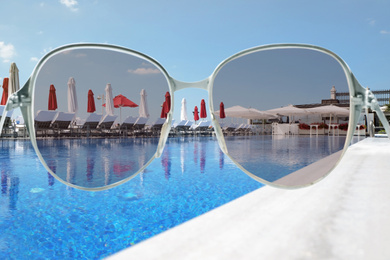 Outdoor swimming pool at sea resort on sunny day, view through sunglasses