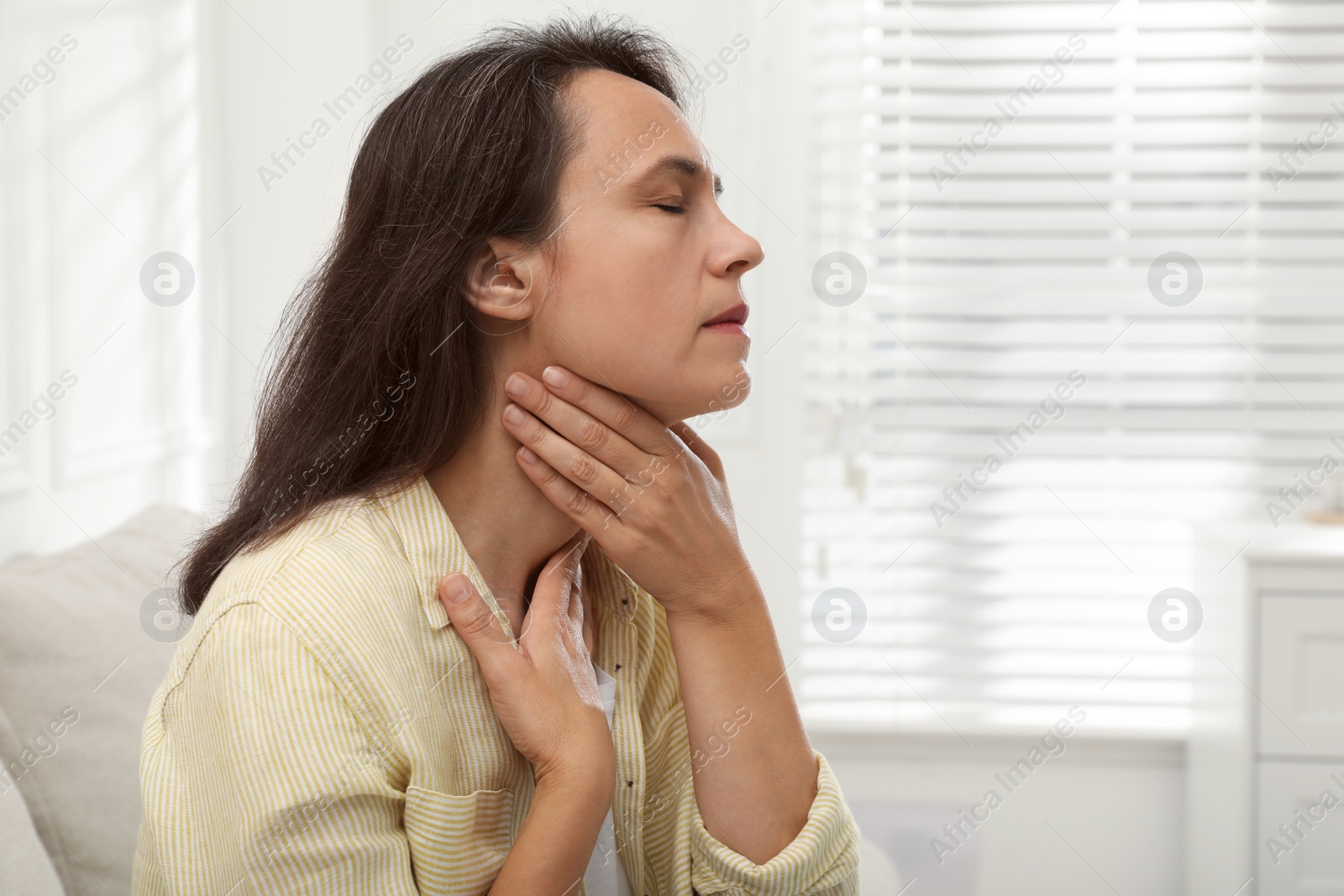 Photo of Mature woman doing thyroid self examination at home. Space for text