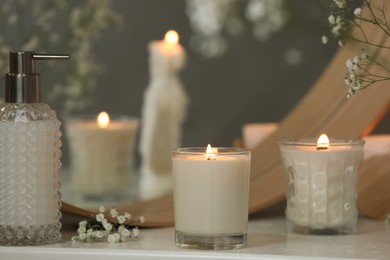 Beautiful burning candles and gypsophila flowers on white table near mirror indoors.