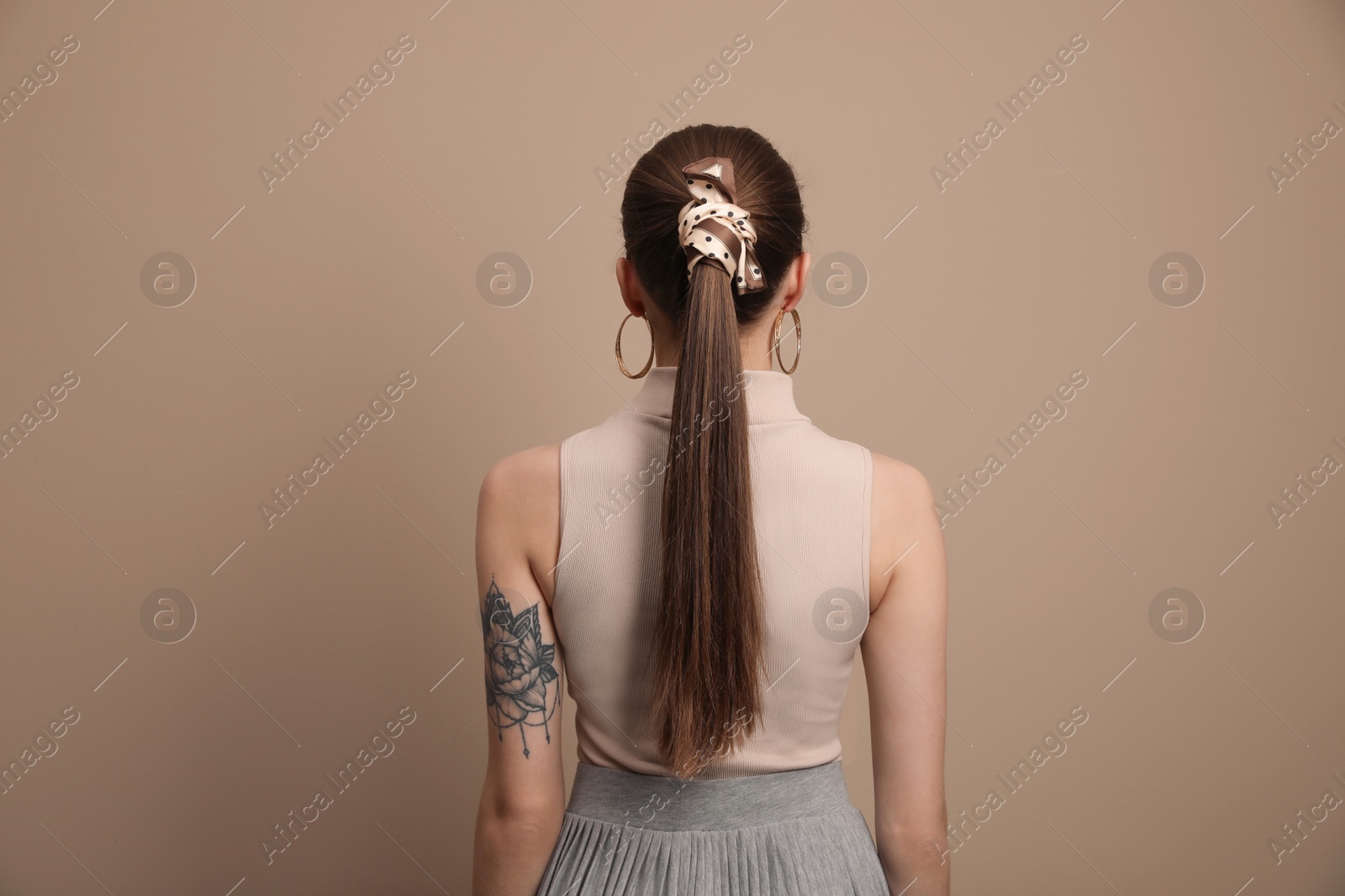 Photo of Young woman with stylish bandana on beige background, back view