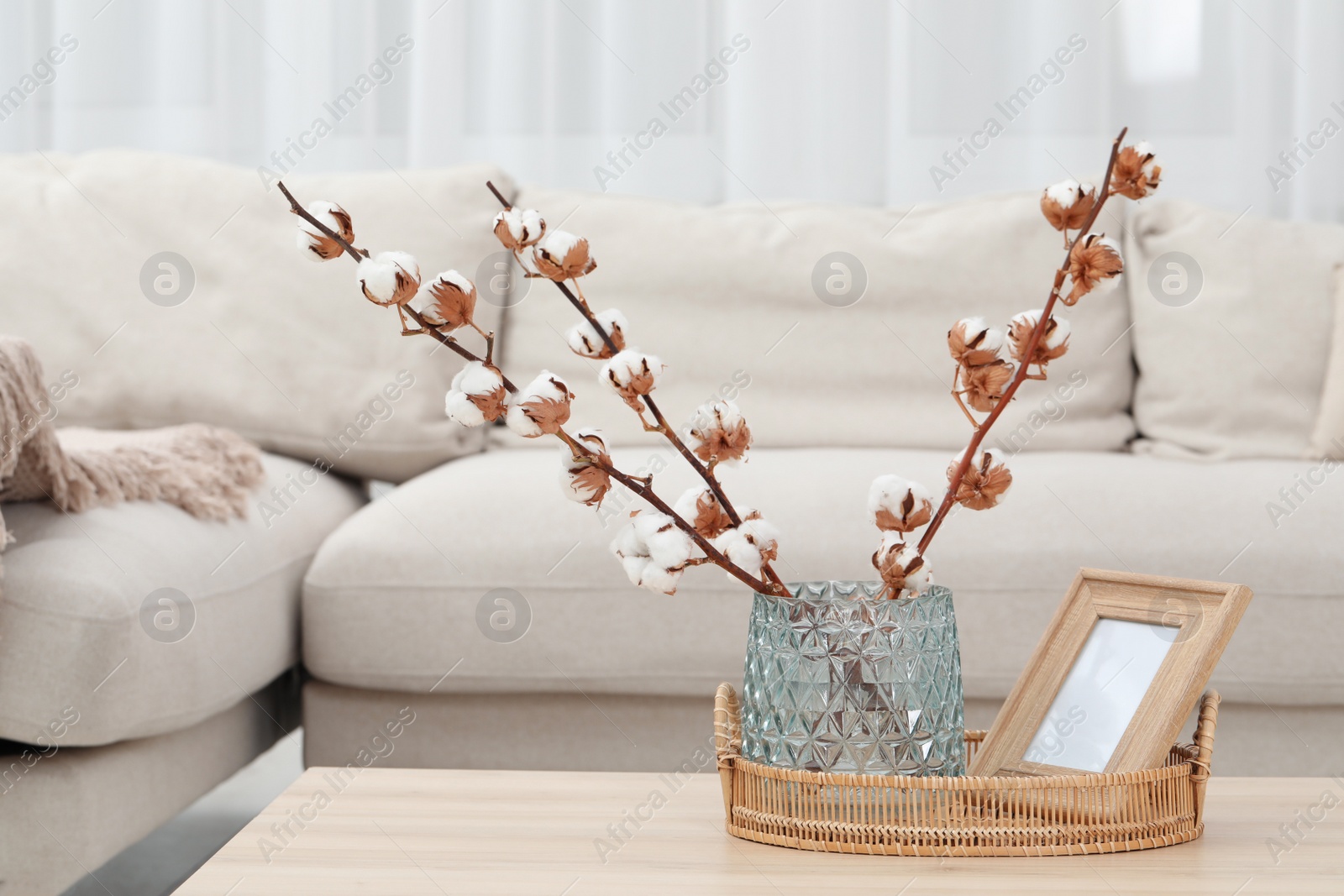 Photo of Wicker basket, wooden frame and cotton branches with fluffy flowers on table in cozy room