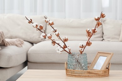 Wicker basket, wooden frame and cotton branches with fluffy flowers on table in cozy room